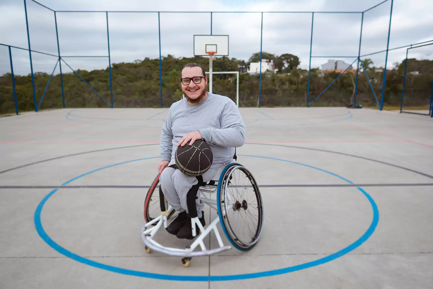 A paraplegic man in a wheelchair is playing basketball outdoors