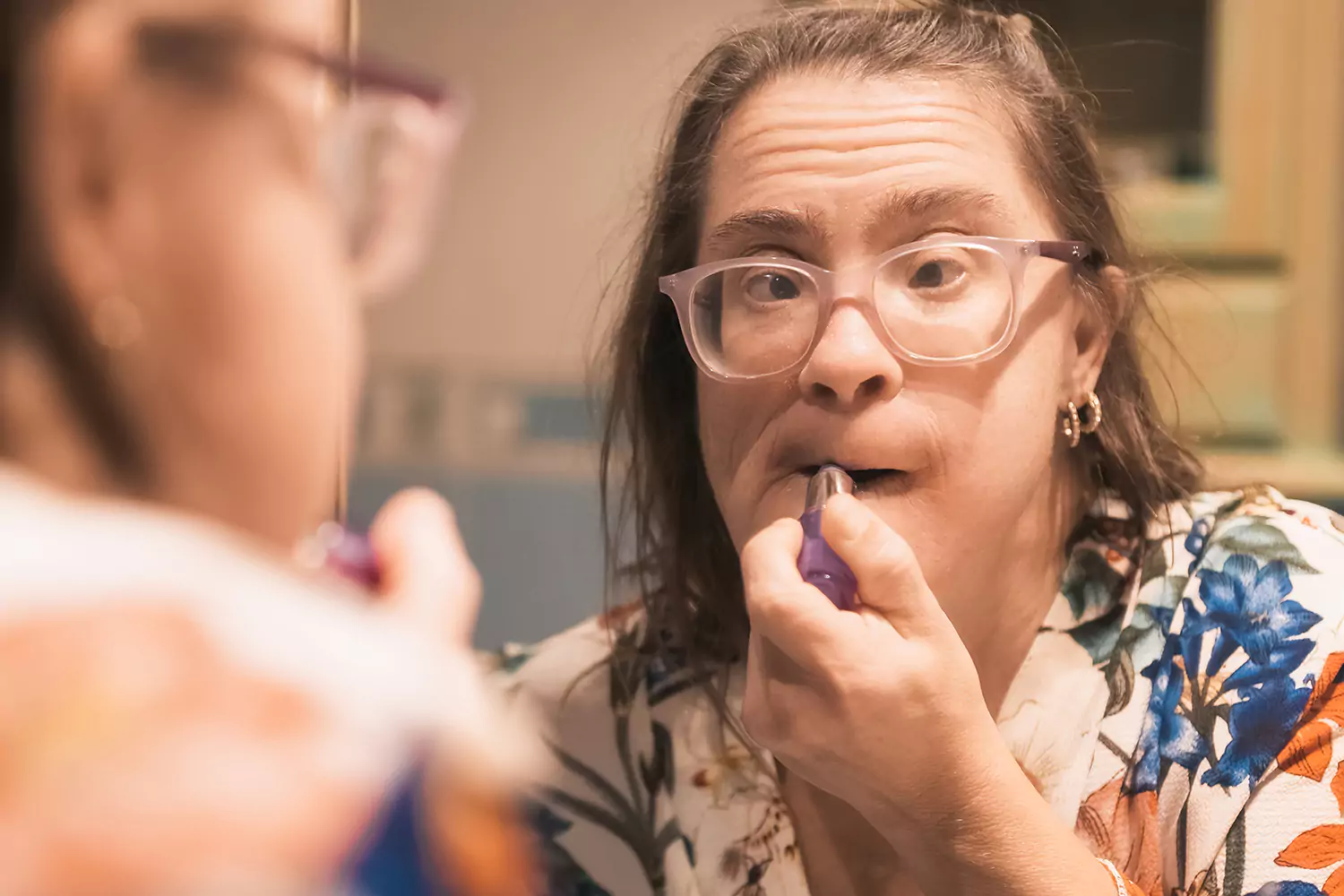 A woman with down syndrome is applying make up in the bathroom